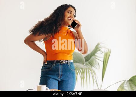 Young businesswoman smiling happily while speaking with her business partners on a phone call. Cheerful female entrepreneur making business plans whil Stock Photo