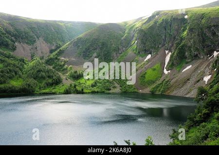 Ripples on the surface of a large lake in a mountain hollow with the remains of snow on the slopes. Ivanovskie lakes, Khakassia, Siberia, Russia. Stock Photo