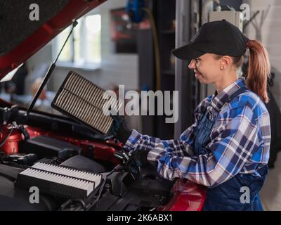 Caucasian female auto mechanic changes the engine air filter in the car. Stock Photo