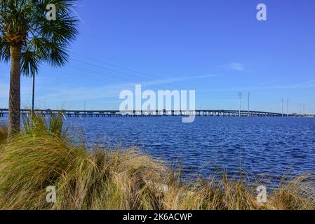 Distant View of the Gilchrist Bridge crossing the Peace River between Port Charlotte and Punta Gorda, Florida framed by palm trees  and wiregrass near Stock Photo