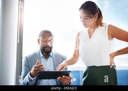 What on earth does this mean. two businesspeople having a discussion in the office while using a digital tablet. Stock Photo