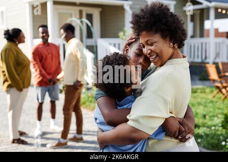Portrait of smiling black woman embracing two sons at family gathering outdoors, copy space Stock Photo