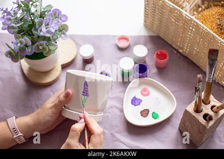 Womens hands paint a white flower ceramic pot on the table. Top view Stock Photo