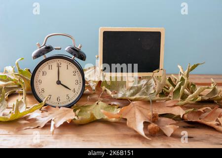 Fall Back Daylight Saving Time. Black alarm clock and autumn leaves on wooden table, copy space Stock Photo