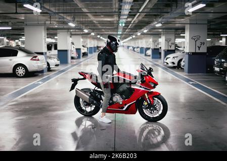 Side view of race motorcycle rider with a helmet in a car parking lot. Stock Photo