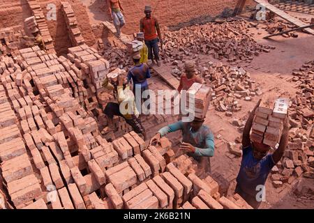 Dhaka, Dhaka, Bangladesh. 13th Oct, 2022. Workers in Dhaka, Bangladesh, carry piles of bricks weighing more than 15 kg on their heads as they are laid out ahead of being baked in a kiln. The labourers ''“ who are paid less than Â£1 a shift ''“ move up to 1,500 bricks a day in sweltering conditions. Around 4, 00,000 low-income migrants arrive in Dhaka from different parts of the country every year to work at brickfields. Long working hours under the scorching sun in the brick fields, massive accumulation of dust, the risk of falling from the trucks and piles of bricks, and carrying excessive l  Stock Photo