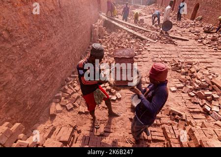 Dhaka, Dhaka, Bangladesh. 13th Oct, 2022. Workers in Dhaka, Bangladesh, carry piles of bricks weighing more than 15 kg on their heads as they are laid out ahead of being baked in a kiln. The labourers ''“ who are paid less than Â£1 a shift ''“ move up to 1,500 bricks a day in sweltering conditions. Around 4, 00,000 low-income migrants arrive in Dhaka from different parts of the country every year to work at brickfields. Long working hours under the scorching sun in the brick fields, massive accumulation of dust, the risk of falling from the trucks and piles of bricks, and carrying excessive l  Stock Photo