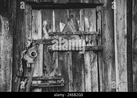 An old gas mask and a dangerous sign with a painted skull hang on the door, gas attack in Ukraine during the war, protective mask, ecology, chemical a Stock Photo