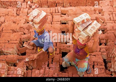 Dhaka, Dhaka, Bangladesh. 13th Oct, 2022. Workers in Dhaka, Bangladesh, carry piles of bricks weighing more than 15 kg on their heads as they are laid out ahead of being baked in a kiln. The labourers ''“ who are paid less than Â£1 a shift ''“ move up to 1,500 bricks a day in sweltering conditions. Around 4, 00,000 low-income migrants arrive in Dhaka from different parts of the country every year to work at brickfields. Long working hours under the scorching sun in the brick fields, massive accumulation of dust, the risk of falling from the trucks and piles of bricks, and carrying excessive l  Stock Photo