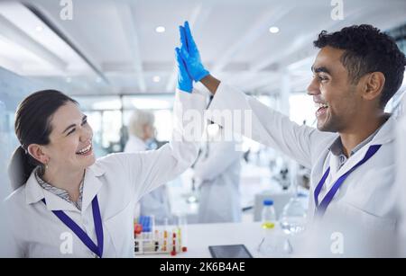 Two happy and cheerful scientists celebrating success with a high five while working together in a lab. Mixed race man and caucasian woman showing Stock Photo