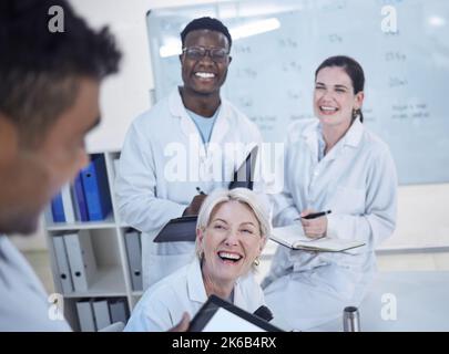Diverse team of young doctors laughing in lab coats discussing work in laboratory Stock Photo