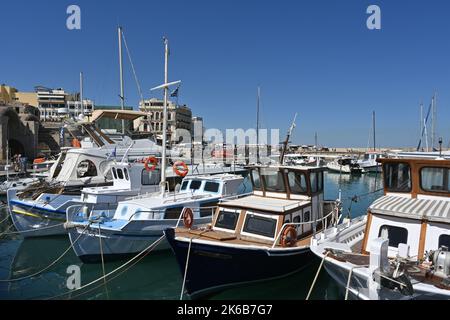 View on wooden fishing boats and white private yachts under blue sky in port of Heraklion near the city center during summer. Stock Photo