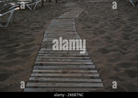 Detail view on wooden sidewalk or footpath in sandy beach in a holiday resort during sunrise. Stock Photo