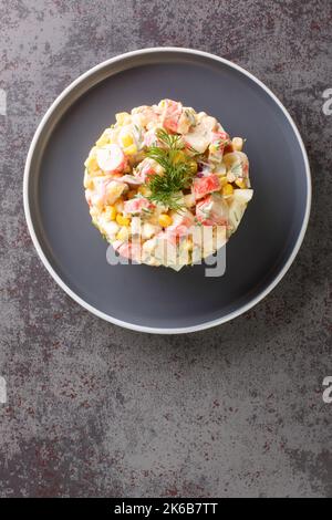 Delicious homemade salad with crab sticks, corn, red onion, hard-boiled eggs and dill closeup in the plate on the table. Vertical top view from above Stock Photo