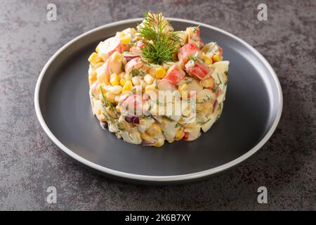 Festive appetizer crab salad with boiled eggs, onion and corn with mayonnaise dressing close-up in a plate on the table. horizontal Stock Photo