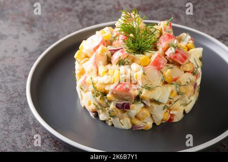 Spicy Salad with crab meat, sweet corn, red onion, hard-boiled eggs and dill closeup in the plate on the table. Horizontal Stock Photo