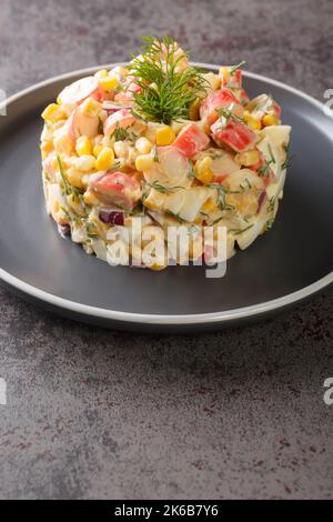 simple salad with crab sticks, eggs, onions and corn dressed with mayonnaise close-up in a plate on the table. vertical Stock Photo