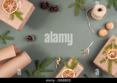 Frame, border made from boxes, craft paper, twine, scissors, dried oranges and natural decor for wrapping XMAS, New Year gifts on green background. Co Stock Photo