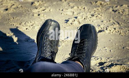 Black men's shoes laced up to the very top with sandy beaches in the background Stock Photo