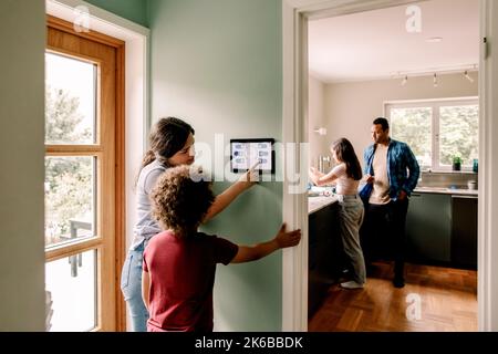 Mother explaining smart home app to son on digital tablet while family in kitchen at home Stock Photo