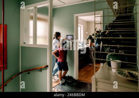Boy using digital tablet with mother while standing near doorway at home Stock Photo