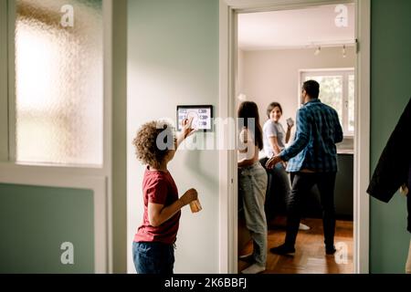 Side view of boy using smart home app on digital tablet while family standing in kitchen Stock Photo