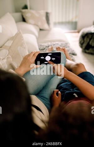 Mother and son using home automation app on smart phone while lying on sofa Stock Photo