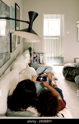 Family using wireless technologies while lying on sofa at home Stock Photo