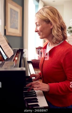 Mature Woman At Home Enjoying Learning To Play Piano Stock Photo