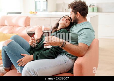 Happy newlywed young couple sitting on the couch and drinking wine for valentines' day - people lifestyle concept Stock Photo