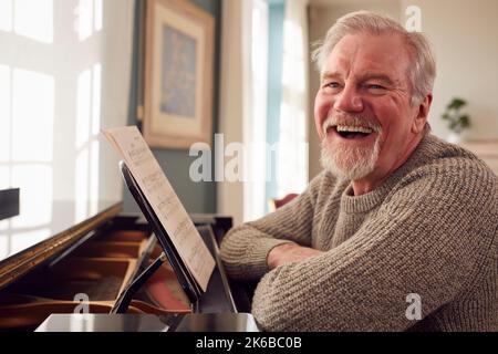 Portrait Of Senior Man At Home Enjoying Learning To Play Piano Stock Photo