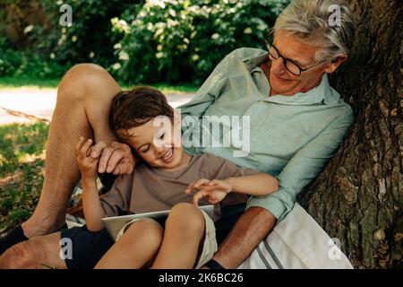Boy using digital tablet while sitting with grandfather at park Stock Photo