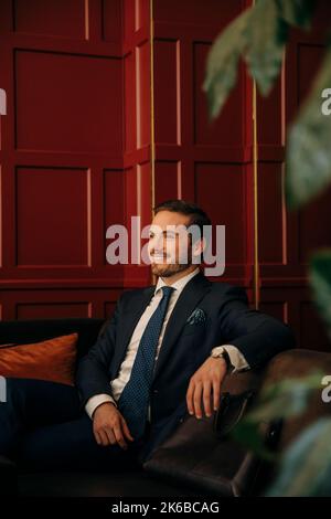 Smiling young businessman sitting on sofa in hotel lounge Stock Photo