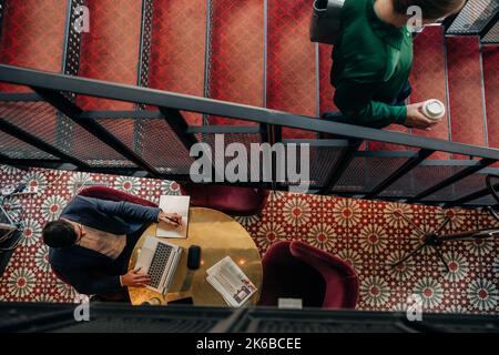 High angle view of businessman using laptop at table while businesswoman moving from steps in hotel Stock Photo