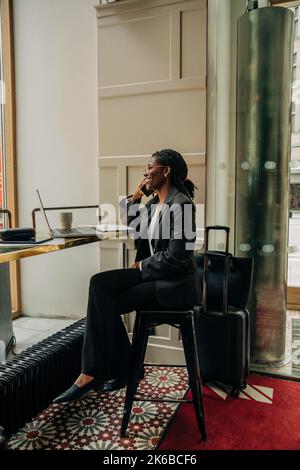 Full length of smiling female entrepreneur talking on mobile phone while sitting with laptop in hotel lounge Stock Photo