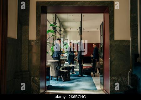 Young businesswoman greeting businessman while standing with colleagues in hotel lounge Stock Photo
