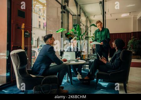 Mature businesswoman discussing ideas with male and female colleagues during meeting in hotel lounge Stock Photo