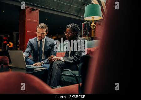 Young businessman discussing over laptop with female colleague sitting in hotel lounge Stock Photo