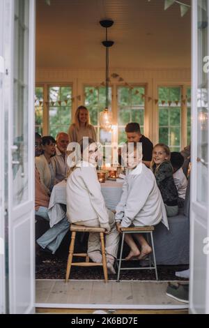 Boy and girl looking over shoulder while sitting on stool at dining table with family Stock Photo