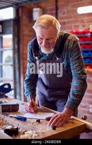 Senior Male Carpenter In Garage Workshop Sketching Out Design On Paper Stock Photo