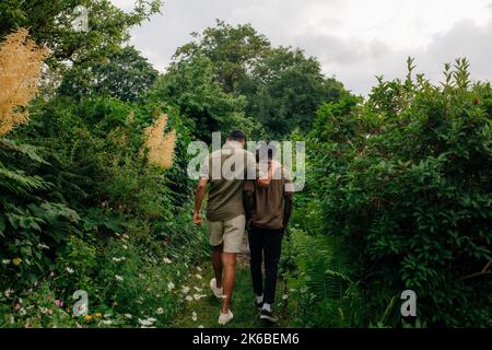 Rear view of male friends walking and talking in garden Stock Photo