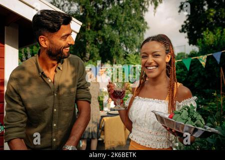 Portrait of happy woman holding plate and drink while standing with male friend Stock Photo