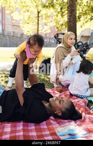 Woman playing with daughter while lying down on picnic blanket at park Stock Photo