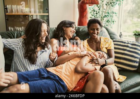 Happy mother and daughters playing with boy while sitting on sofa at home Stock Photo