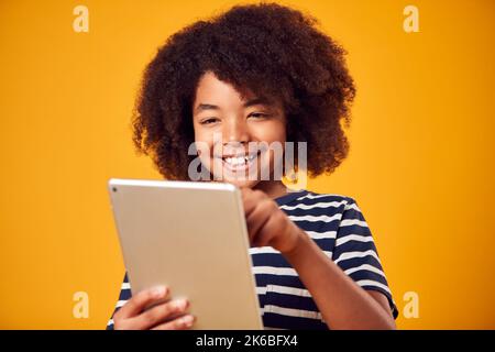 Studio Portrait Of Boy Playing Game On Digital Tablet Against Yellow Background Stock Photo