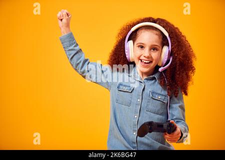 Studio Portrait Of Girl With Headphones Playing Computer Game Against Yellow Background Stock Photo