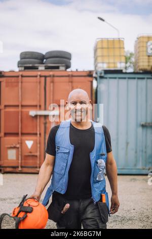 Portrait of happy bald construction worker with hardhat walking at site Stock Photo