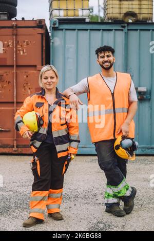 Full length of smile male and female construction workers in reflective clothing standing at site Stock Photo