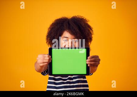 Studio Portrait Of Boy Using Digital Tablet With Green Screen Against Yellow Background Stock Photo