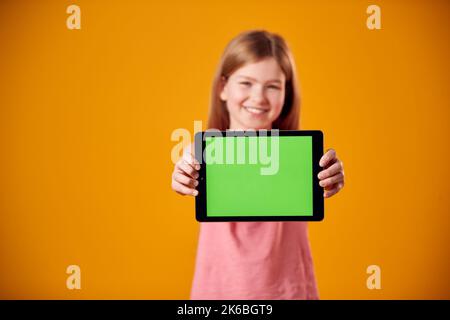 Studio Portrait Of Girl Using Digital Tablet With Green Screen Against Yellow Background Stock Photo